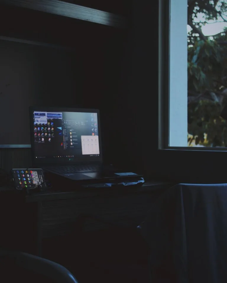 Notebook aberto e iluminado numa mesa às escuras, sem ninguém por perto