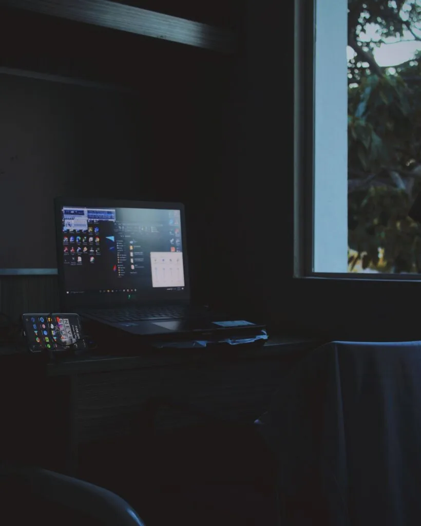 Notebook aberto e iluminado numa mesa às escuras, sem ninguém por perto